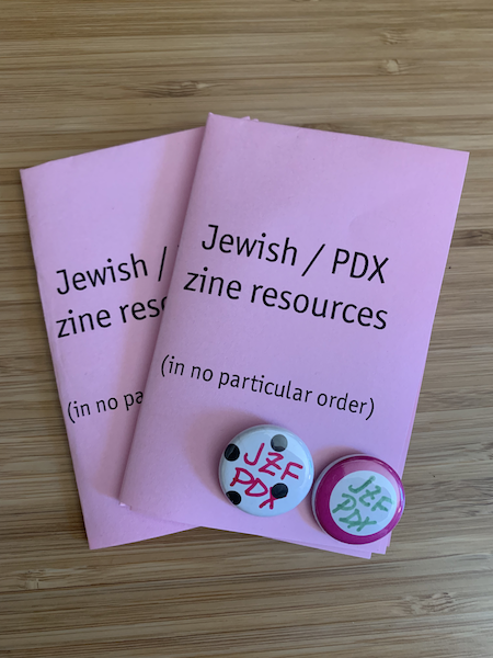 Two one-inch button pins reading "JZF PDX" and two pink mini-zines titled "Jewish/PDX zine resources (in no particular order)"